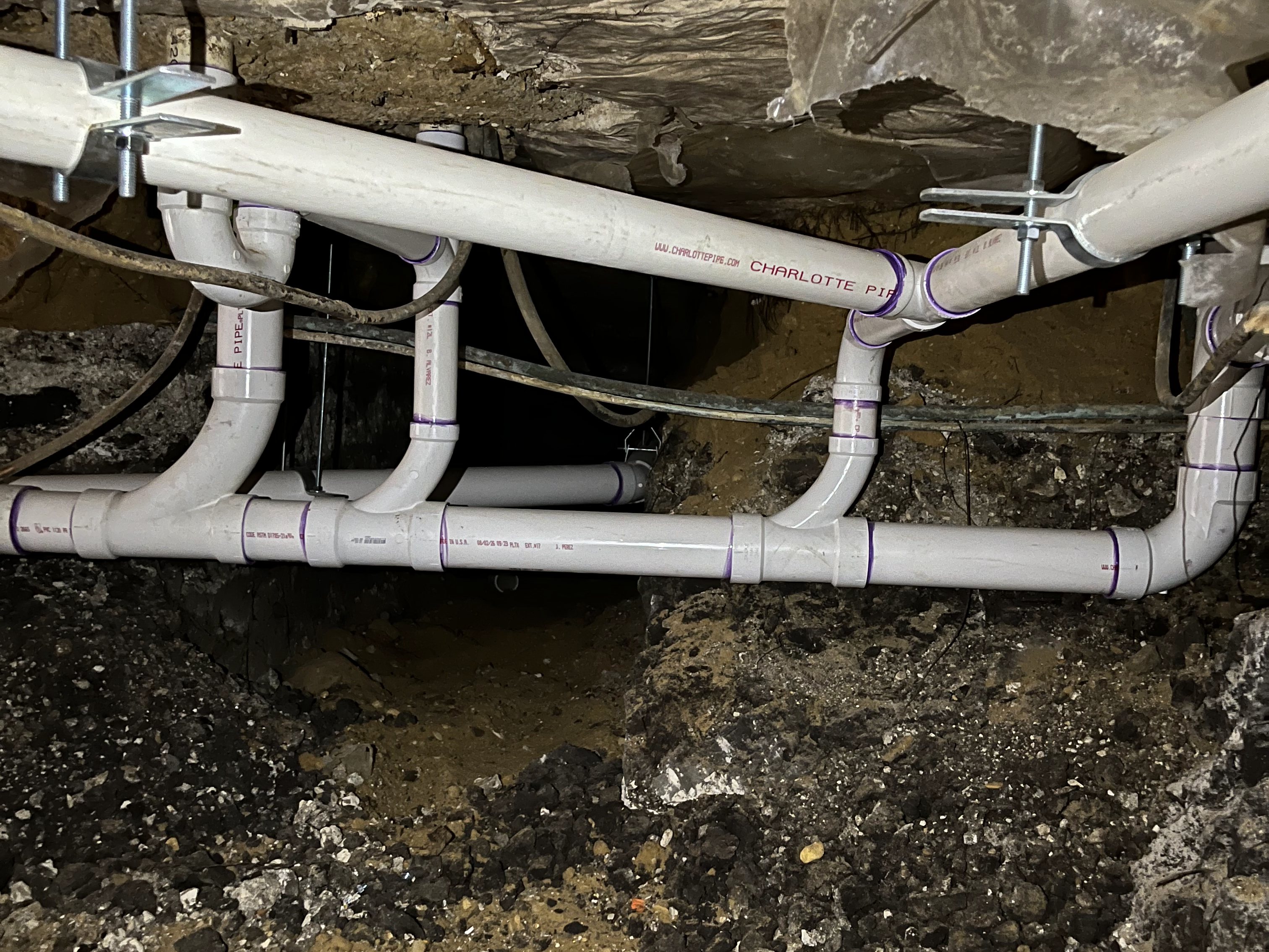 New PVC drain manifold hung in a tunnel beneath a house foundation