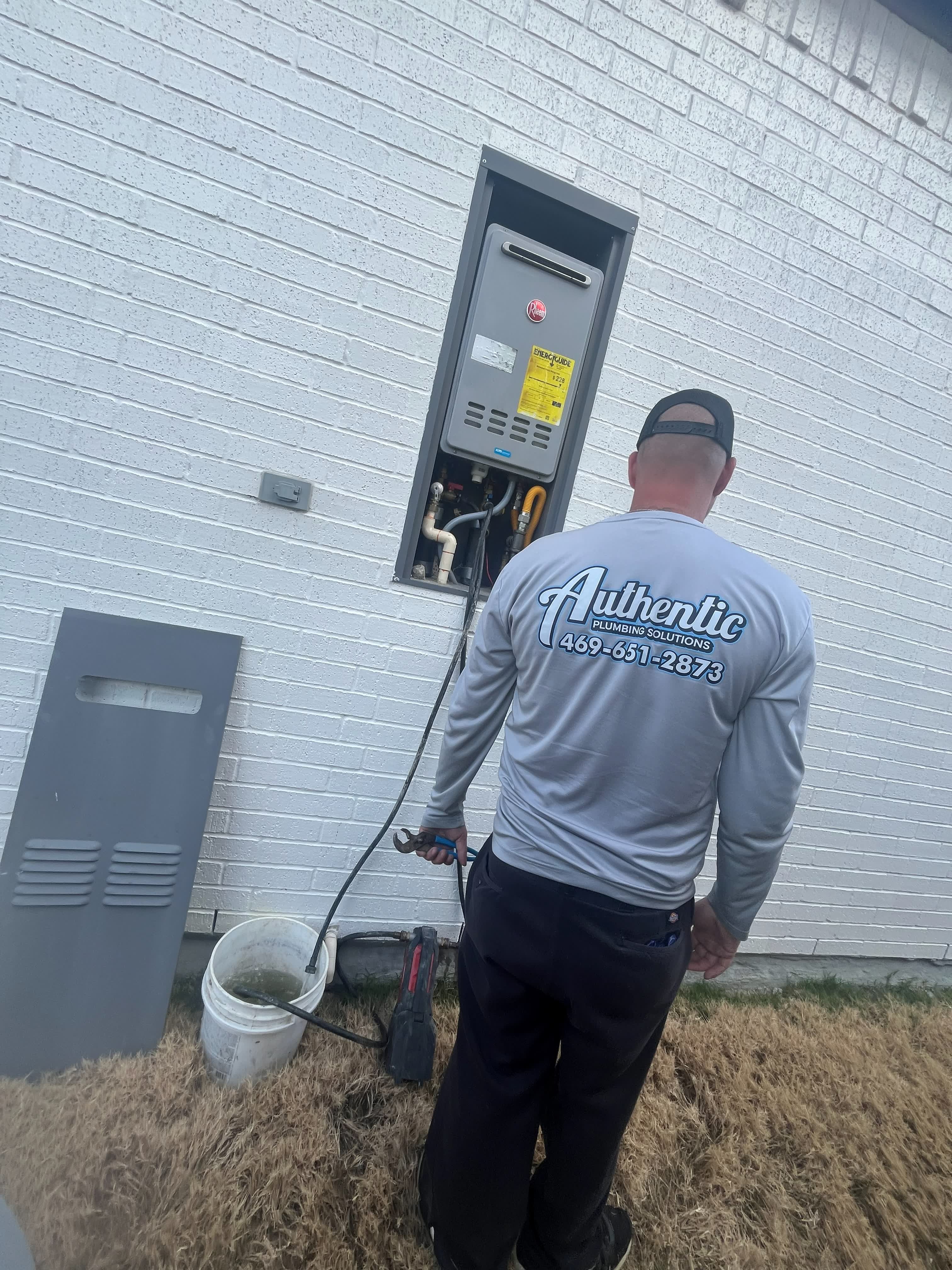 Authentic Plumbing technician flushing an outdoor tankless water heater