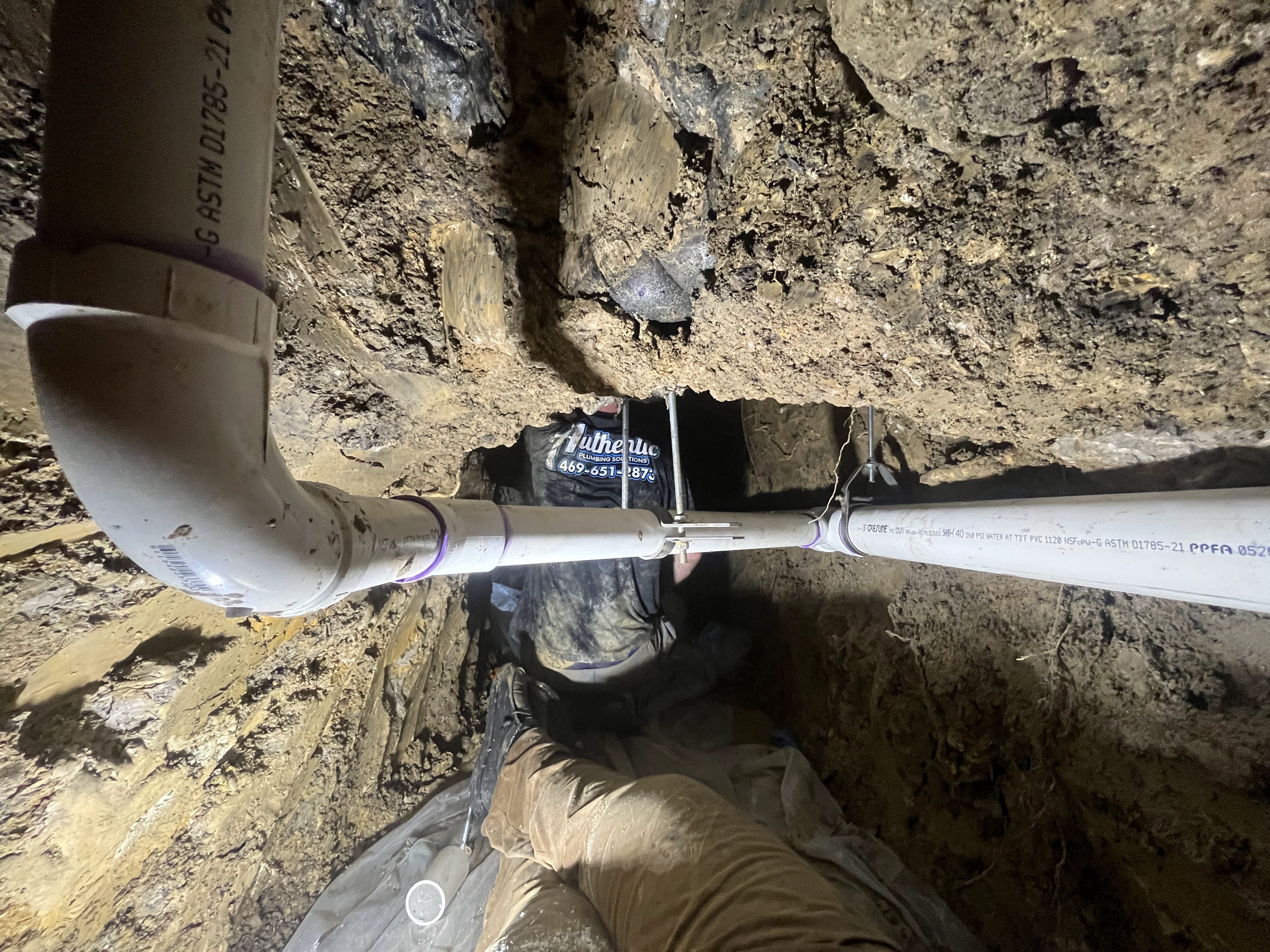Authentic Plumbing technician working inside a tunnel dug beneath a house foundation