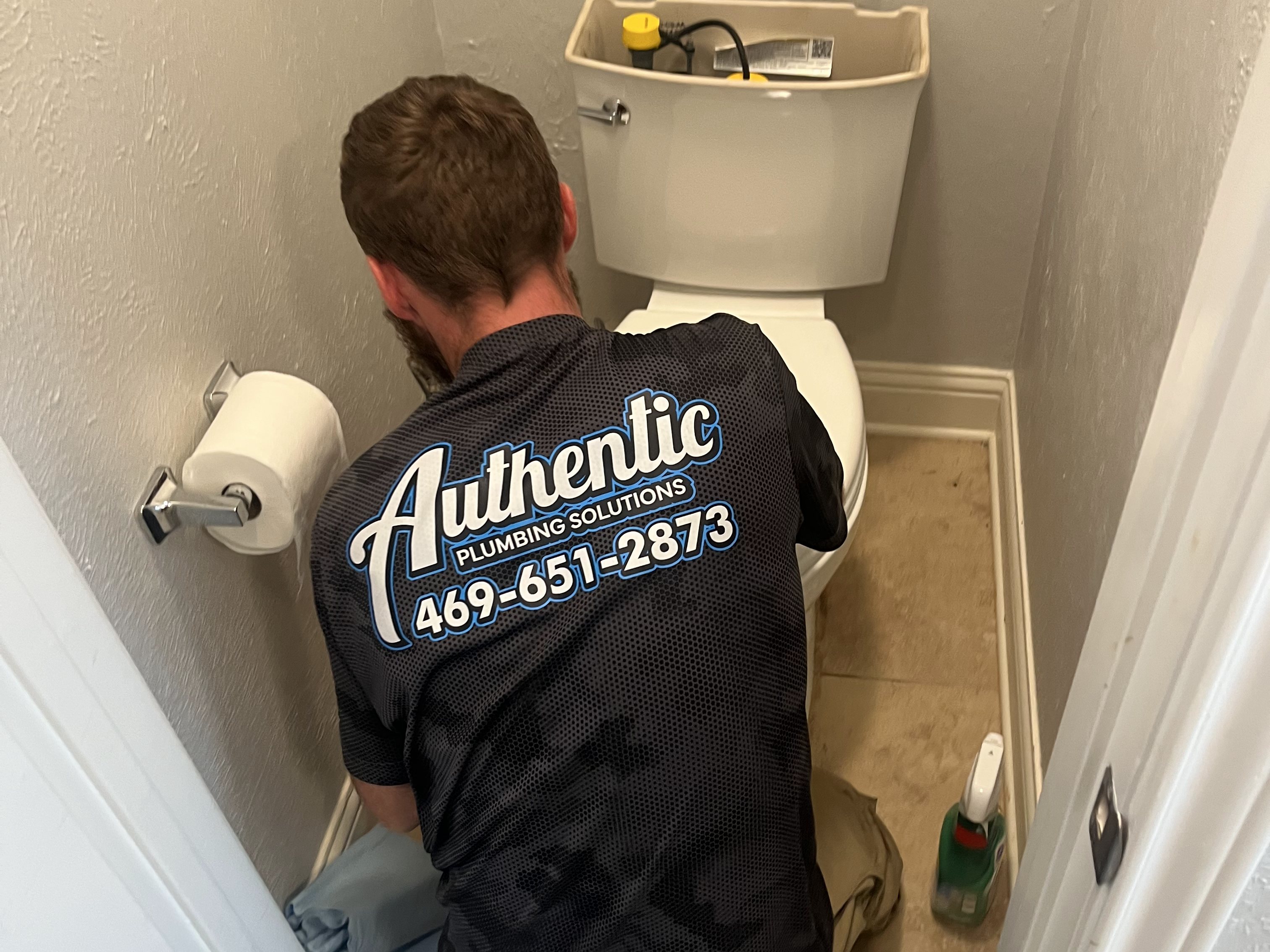 Authentic Plumbing technician servicing a toilet, with floor protection down